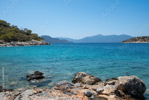 Greece Aponisos beach Agistri island. Rocky land, pine tree, clear sea water, blue sky background.