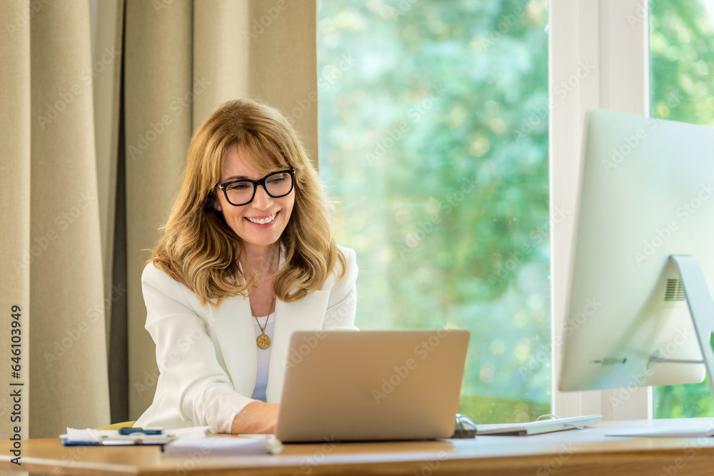 Blonde haired businesswoman sitting at her desk and working on her laptop Blonde haired businesswoman sitting at her desk and working on her laptop