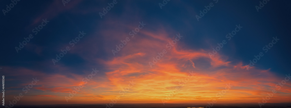 Fire on the sky: Aerial, long panoramic view of colorful, orange and red colored streakes of cirrus clouds on deep blue evening sky.  Ideal for sky replacement projects, no obstacles in the front. 