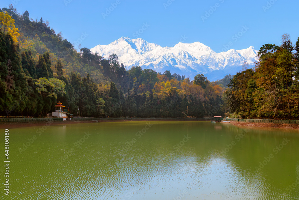Scenic mountain lake surrounded by trees with a view of the Kanchenjunga Himalaya mountain range at Sikkim, India.