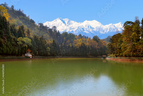 Scenic mountain lake surrounded by trees with a view of the Kanchenjunga Himalaya mountain range at Sikkim, India.