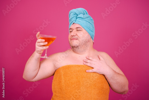 Early morning. Funny fat man is preparing for a party and drinking a cocktail. Pink background.