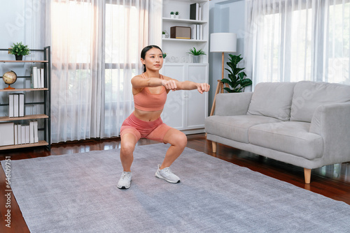 Fototapeta Naklejka Na Ścianę i Meble -  Vigorous energetic woman doing exercise at home. Young athletic asian woman strength and endurance training session as home workout routine with squat.