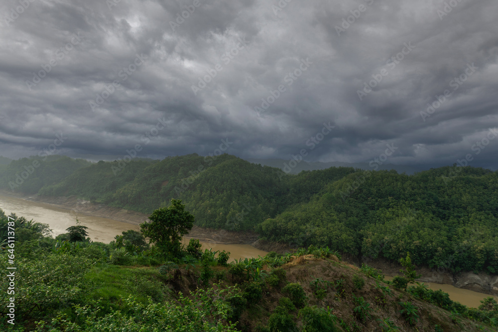 During the rainy season, the thick green hills blend into the thick black clouds in the sky. Sangu river flows below. Hilly region of Bandarban district of Bangladesh. During the rainy season, the thick green hills blend into the thick black clouds in the sky. Sangu river flows below. Hilly region of Bandarban district of Bangladesh.