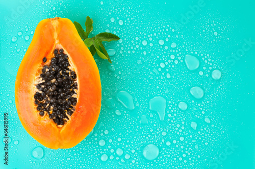 Papaya fruit on blue background with water drops, fresh exotic fruits border design. Half of fresh organic Papaya exotic fruit with leaf close up. Top view