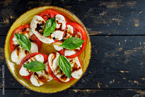 Italian Caprese Salad with sliced tomatoes, mozzarella and basil on dark boards. Copy space