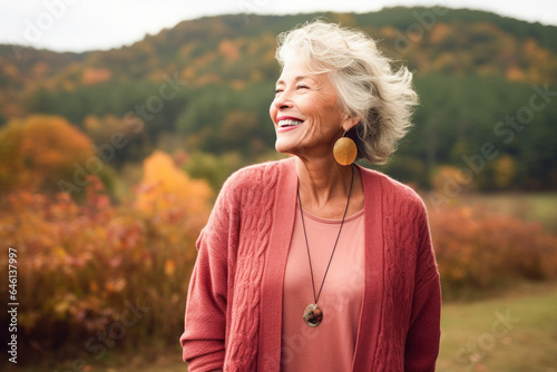 Portrait in the forest of a pleased 70 years old woman. Joyful woman in an outdoor fall scenery having fun at the autumn season. 