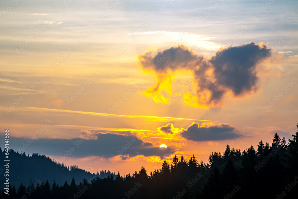 Colorful clouds in the sky at sunset against the backdrop of a mountainous forest area.
