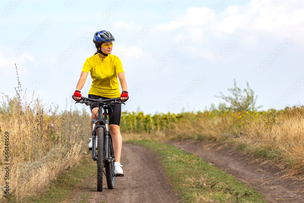 beautiful woman cyclist in a yellow shirt rides a bicycle along a field road. sports, hobbies and entertainment for health beautiful woman cyclist in a yellow shirt rides a bicycle along a field road. sports, hobbies and entertainment for health