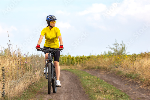beautiful woman cyclist in a yellow shirt rides a bicycle along a field road. sports, hobbies and entertainment for health