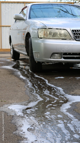 vertical frame with a wet gray car washed at home in the courtyard of a private house with a stream of soapy water flowing down the asphalt, a car after a home wet cleaning in the courtyard