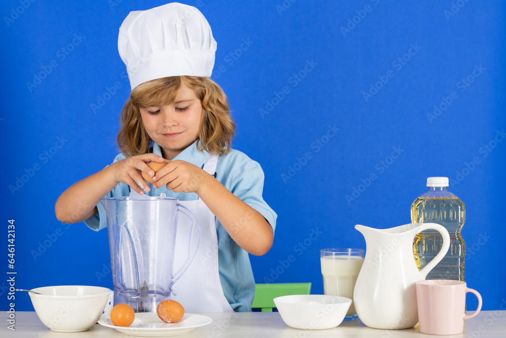 Kid boy in chef hat and apron cooking preparing meal. Little cook with vegetables at kitchen. Natural kids food. Kid boy in chef hat and apron cooking preparing meal. Little cook with vegetables at kitchen. Natural kids food.