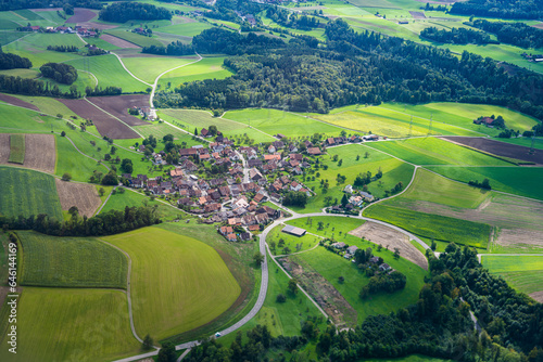 Aerial view of a small village in the middle of green fields in Zurich district photographed on a sunny summer day. Zurich, Switzerland, Europe.