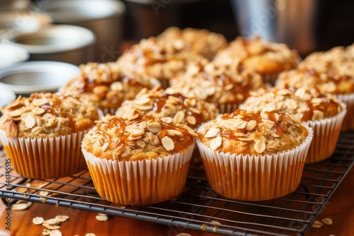 A tray of freshly baked oatmeal muffins, cooling on a wire rack. The muffins are golden brown and fluffy, with a moist and flavorful center. They are topped with a generous amount of crunchy oats 