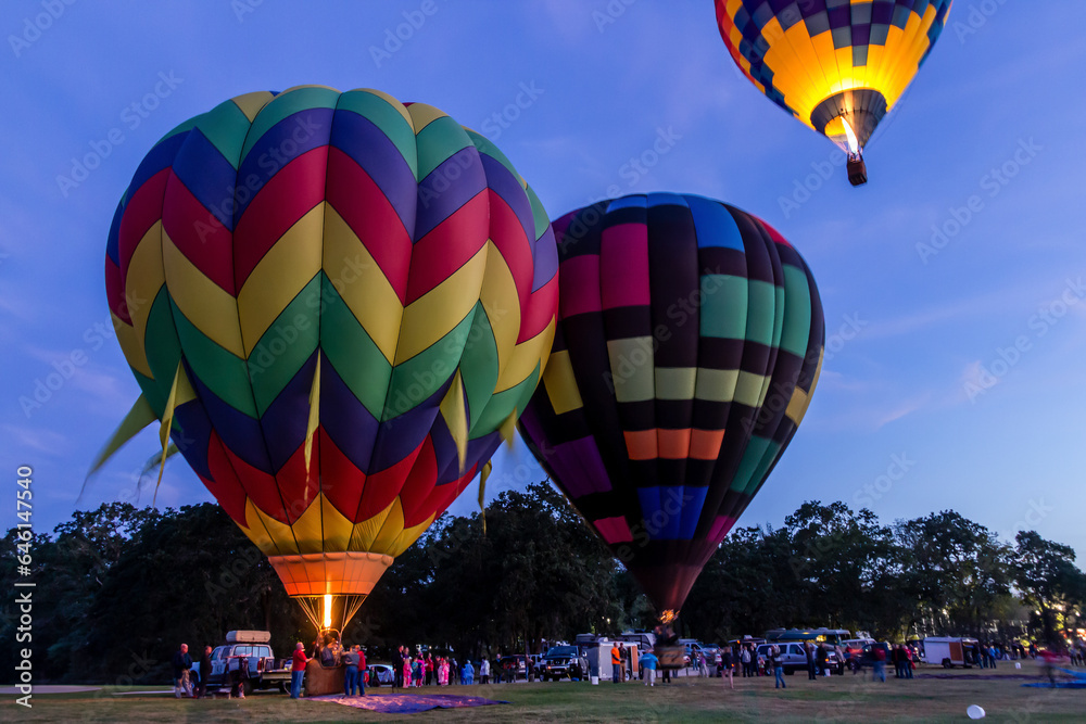 Obraz premium 3 balloons ready to launch a daylight patrol. One is already in the air with its gas lit. The other two are on the ground fully inflated. They are brightly colored.