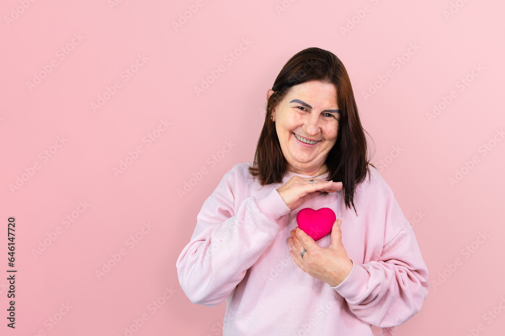 A radiant mature woman, smiling with strength and joy, holds a pink resin heart: a symbol of hope and support for breast cancer awareness, ideal for October Pink campaign. A radiant mature woman, smiling with strength and joy, holds a pink resin heart: a symbol of hope and support for breast cancer awareness, ideal for October Pink campaign.