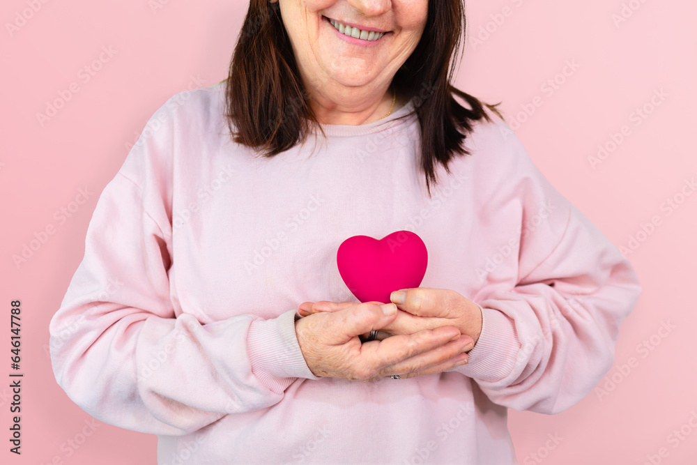 A mature woman smiles while holding a pink resin heart, symbolizing hope and support for breast cancer awareness, ideal for October Pink campaigns A mature woman smiles while holding a pink resin heart, symbolizing hope and support for breast cancer awareness, ideal for October Pink campaigns