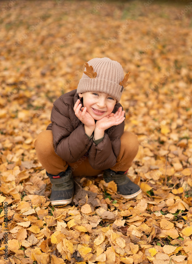 Little cute boy with deer horns made of oak leaves sits in yellow foliage Little cute boy with deer horns made of oak leaves sits in yellow foliage
