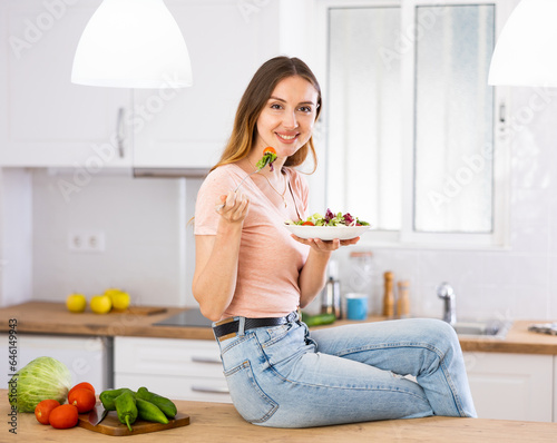 Young smiling girl enjoying salad sitting on kitchen table