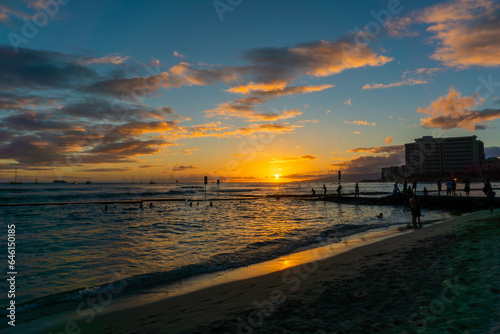 Golden Sunset Over Waikiki Beach in Oahu, Hawaii, With Silhouette of Unidentifiable Visitors on Beach and in the Waters © ronniechua