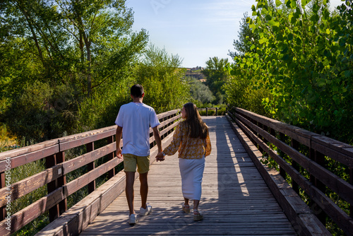 boy and girl in love walking along a wooden bridge holding hands on a sunny day © Avelino