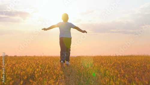 Child boy runs on field on grass at sun. Dream of child to fly, arms like airplane wings. Childhood dream concept. Healthy little child plays at sunset. Kid runs across field. Happy family concept