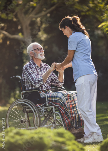 Nurse comforting senior man in wheelchair in park