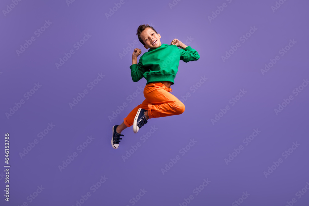 Photo of overjoyed nice boy wear green trendy outfit raise fist have fun enjoy rejoice shopping sale isolated on purple color background