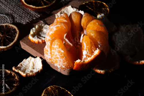 Half peeled tangerine in a darkfood environment with dried citrus peels and slices.