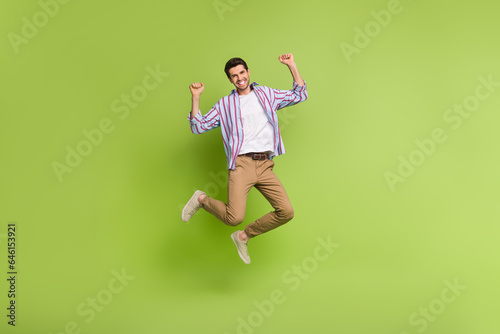 Full size body photo of crazy active youngster man jumping raised fists up big discount promo shopping isolated on green color background