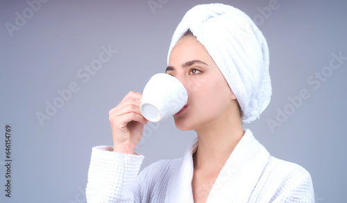 Morning coffee. Close up portrait of young woman with cup of drink coffee. Smiling girl drinking coffee isolated on gray studio background. Pretty woman in bathrobe and towel with cup of hot coffee.