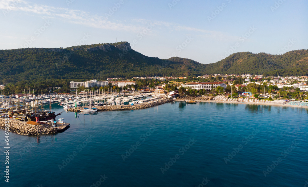 Picturesque summer aerial view of coastal area of Kemer and marina with moored yachts on Mediterranean coast on background of Taurus Mountain range, Antalya province. Famous resort on Turkish Riviera