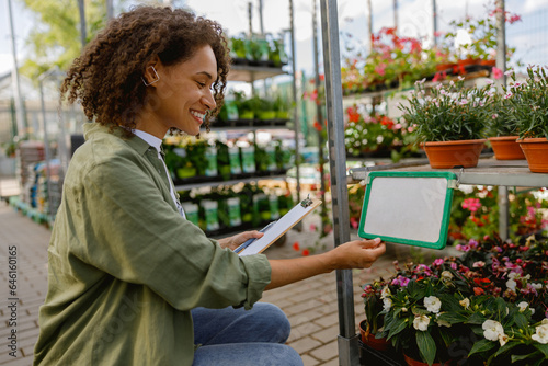 Smiling woman florist with clipboard conducts inventory in flower garden center © Kostiantyn