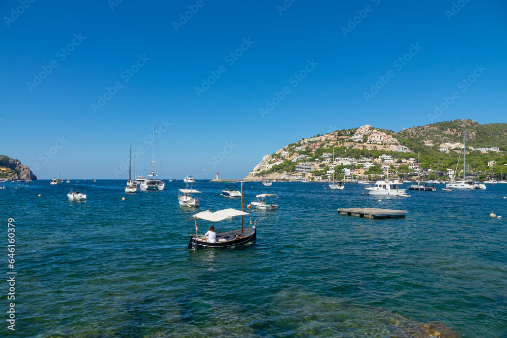 View of the Port d’Andratx (Mallorca, Spain) with houses on the hills, a lighthouse and recreational and fishing boats in the sea on a sunny summer morning