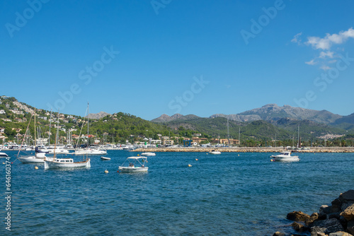 View of the Port d’Andratx (Mallorca, Spain) with houses on the hills, a lighthouse and recreational and fishing boats in the sea on a sunny summer morning