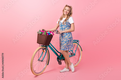 Full size portrait of stunning positive girl drive bicycle fresh flowers basket isolated on pink color background © deagreez