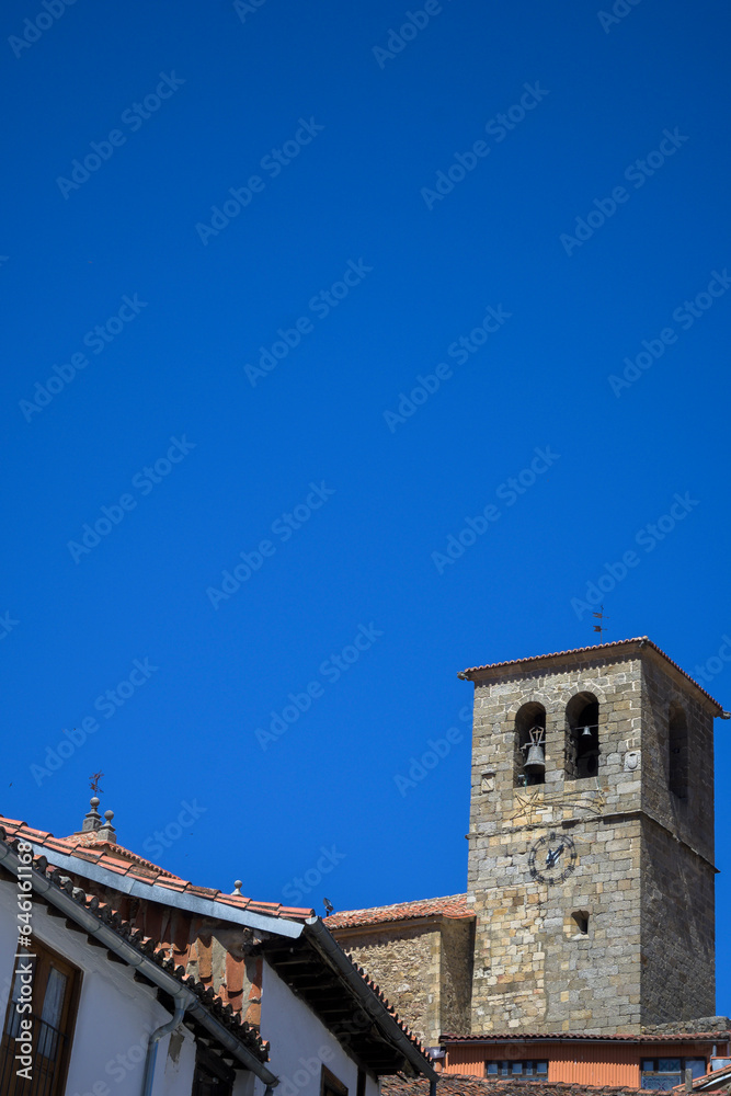 Church stone tower with bell tower and clock with blue sky in vertical in Hervas