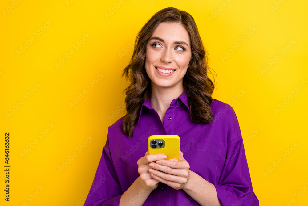 Portrait of gorgeous positive girl with curly hair wear violet blouse look empty space hold smartphone isolated on yellow background Portrait of gorgeous positive girl with curly hair wear violet blouse look empty space hold smartphone isolated on yellow background