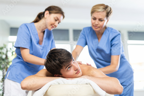 Two women doing back massage to man lying on massage table in a spa salon