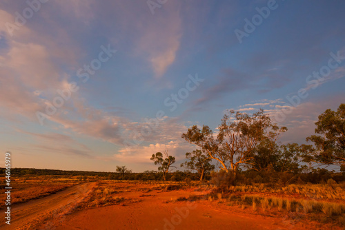 A dirt road in typical semi arid country at sunset with sky and clouds in Currawinya National Park in Australia