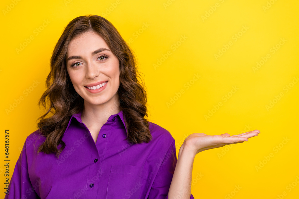 Portrait of good mood nice girl with curly hair wear violet blouse arm demonstrate offer empty space isolated on yellow background Portrait of good mood nice girl with curly hair wear violet blouse arm demonstrate offer empty space isolated on yellow background