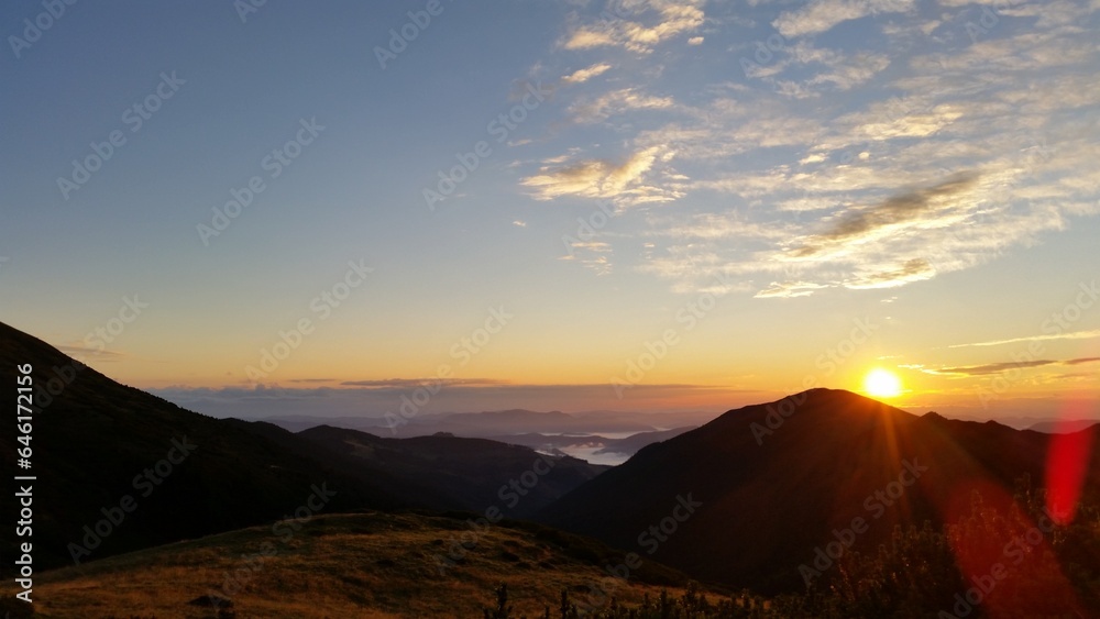 The sun sets slowly behind the mountain range, casting a warm orange glow across the landscape..