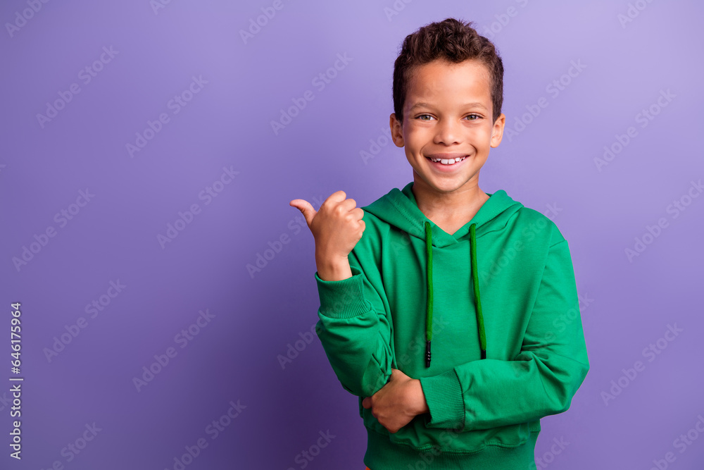 Photo of charming cool small boy wear green sweatshirt showing thumb empty space isolated violet color background Photo of charming cool small boy wear green sweatshirt showing thumb empty space isolated violet color background