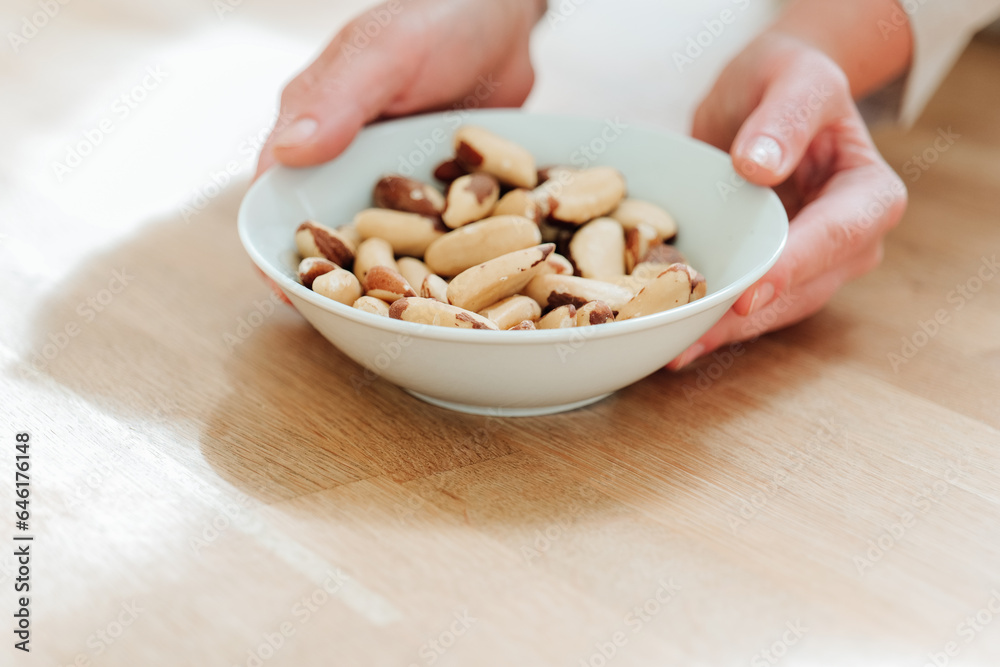 Brazil nuts in the diet. Healthy fats in the diet. Brazil nuts in a white ceramic cup in hand on a wooden table.Nuts and seeds.Useful healthy snack. Brazil nuts in the diet. Healthy fats in the diet. Brazil nuts in a white ceramic cup in hand on a wooden table.Nuts and seeds.Useful healthy snack.