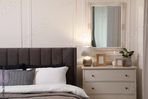 Stylish bedroom interior with large comfortable bed and chest of drawers