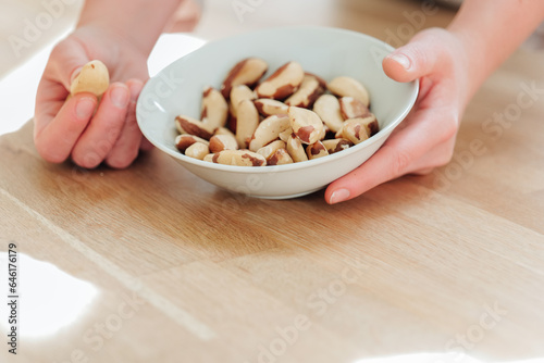 Nuts and seeds. Brazil nuts in a white ceramic cup in hand on a wooden table. Healthy fats in the diet. hand takes brazil nuts from a plate close-up.Useful healthy snack. Brazil nuts in the diet.