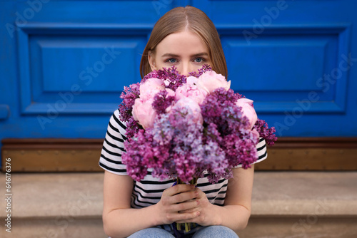 Beautiful woman with bouquet of spring flowers near building outdoors