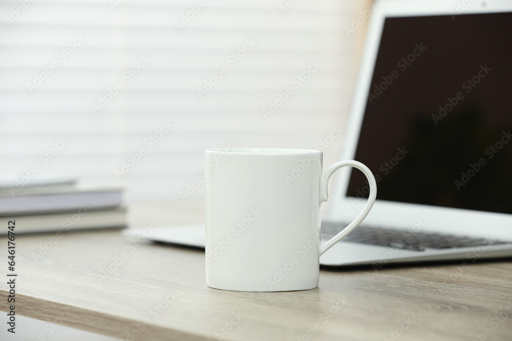 White ceramic mug and laptop on wooden table indoors White ceramic mug and laptop on wooden table indoors