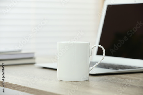 White ceramic mug and laptop on wooden table indoors