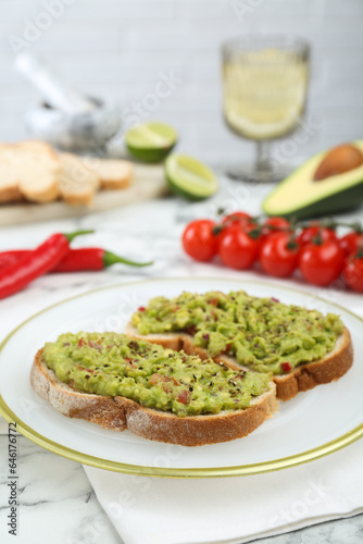Delicious sandwiches with guacamole and ingredients on white table